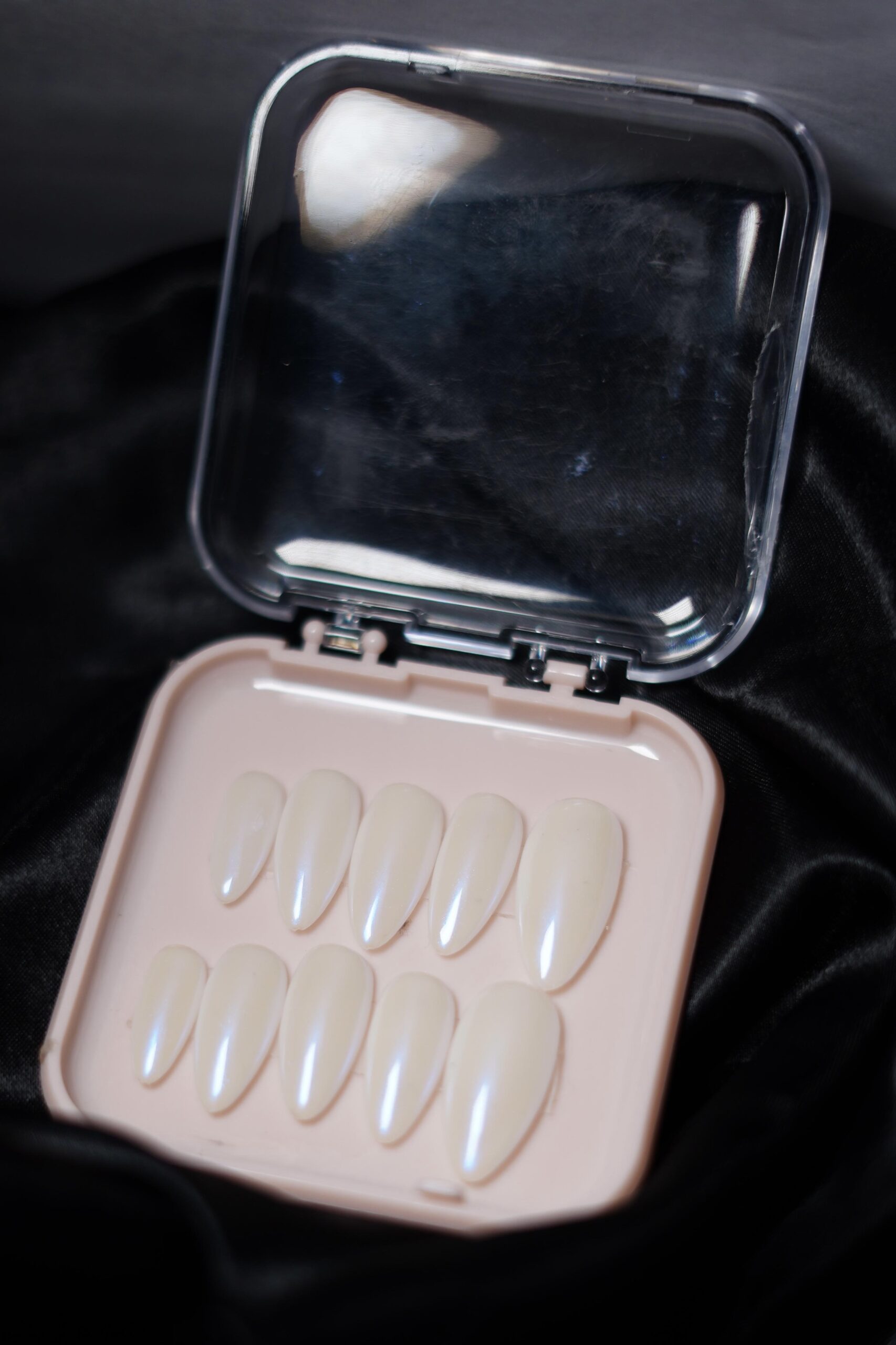 A hand wearing glossy pearl white almond-shaped press-on nails with a soft iridescent shimmer, giving a classy and elegant look.